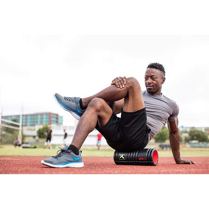 "A man on a track uses the TriggerPoint GRID X® Foam Roller to break through dense muscle tissue for a deep tissue massage."